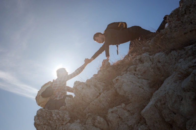 Help and assistance concept. Silhouettes of two people climbing mountains and helping against the blue sky. Walk in the clouds. Discovery Travel Direction Concept
